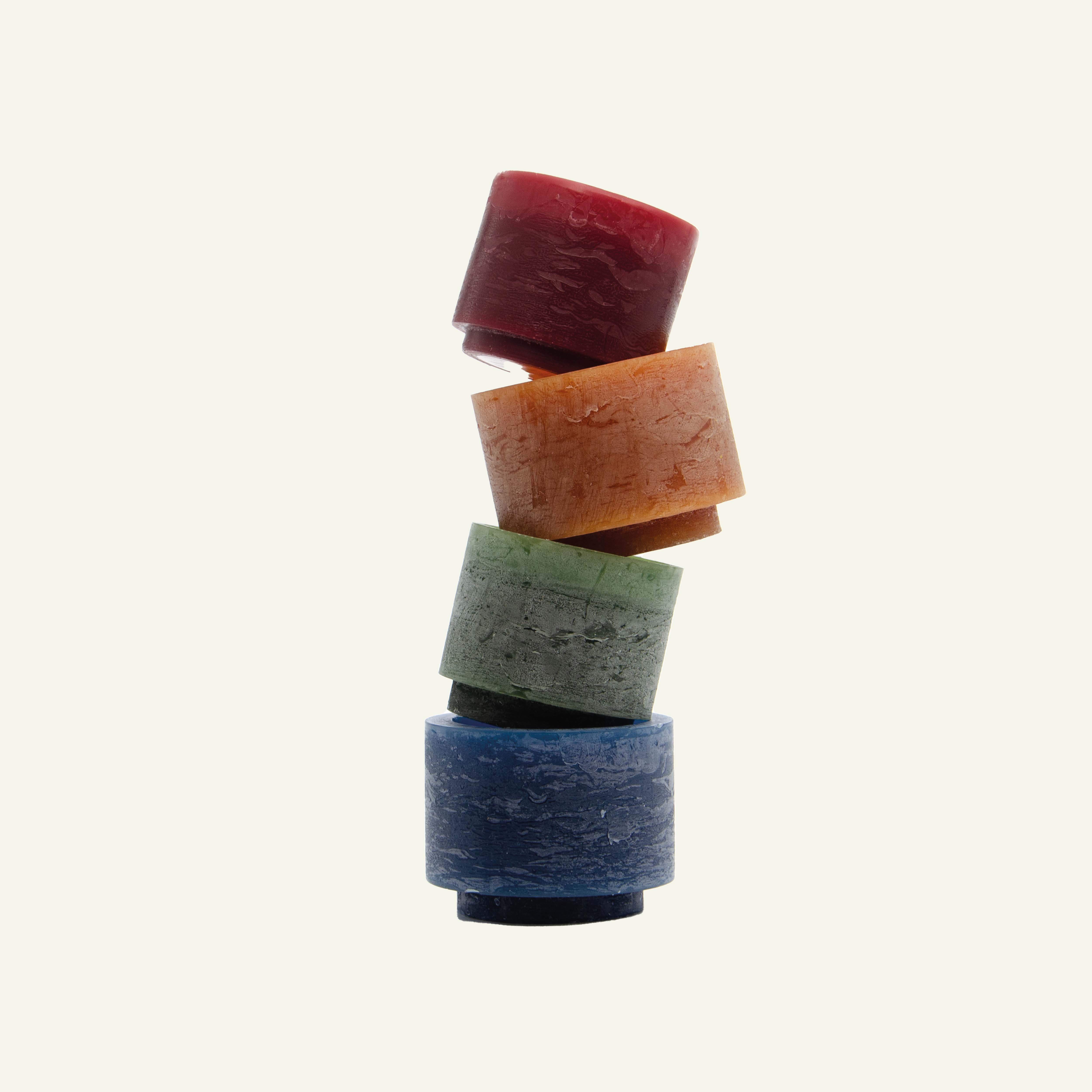 Een kaarsen toren van een blauwe, groene, bruine en bordeaux Stan Editions kaars die op een speelse manier op elkaar zijn gestapeld met een witte achtergrond.